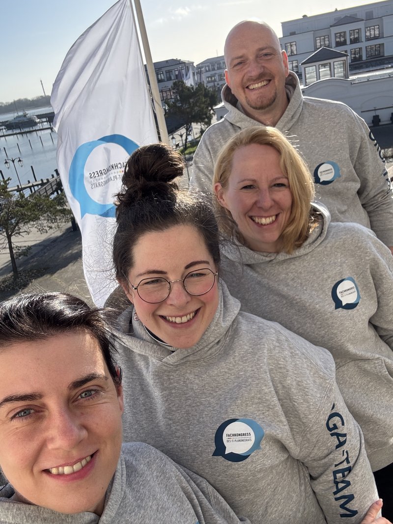 4 Teilnehmer des 14. Fachkongresses außen vor einer Flagge des Fachkongresess