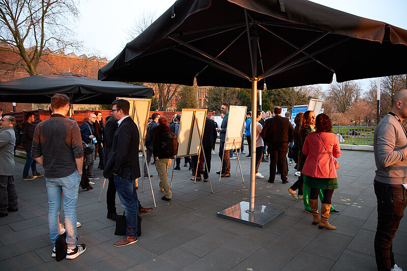 Postersession draußen: Leinwände auf Staffeleien mit Menschen, die darum stehen