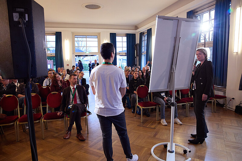 Blick über die Schulter von 2 Referenten mit Flipchart aufs Publikum