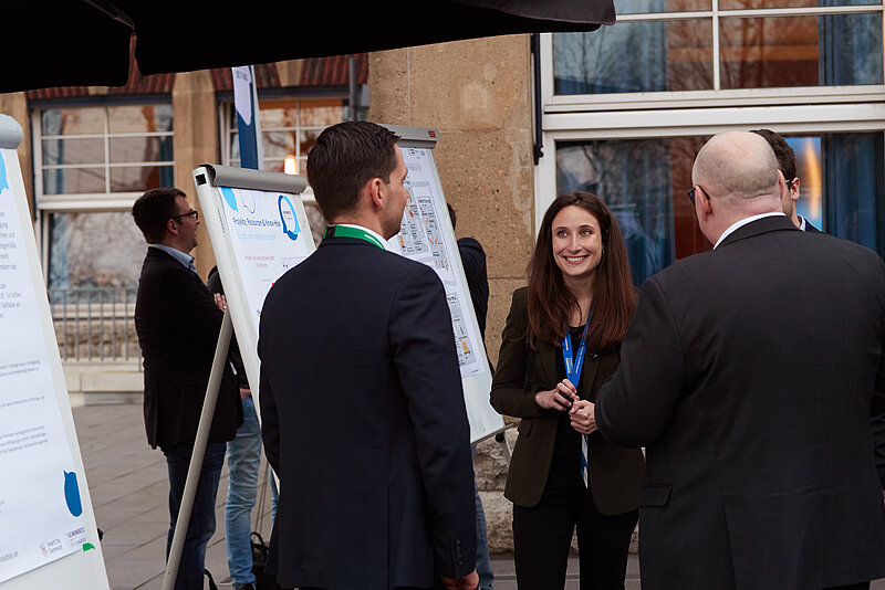 3 Personen unterhalten sich vor einem Flipchart