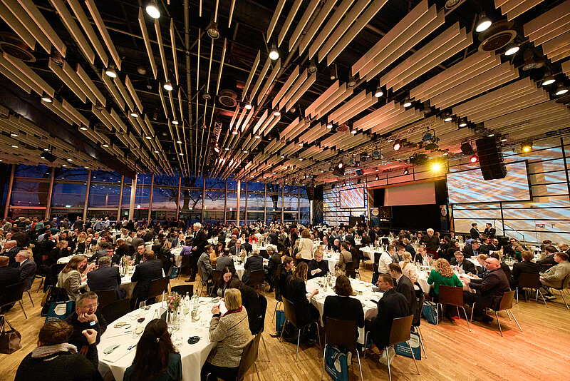 Blick in den Saal mit festlich gedeckten Tischen und Menscen bei der Abendveranstaltung