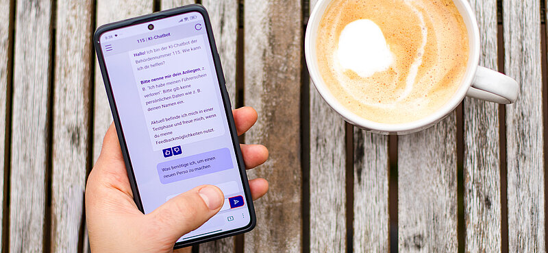 Ansicht einer Hand, die ein Handy mit dem 115-Chatbot auf dem Bildschirm hält.
