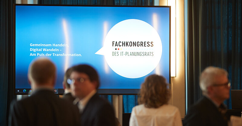 Bildschirm mit dem Fachkongress-Logo, davor Menschen