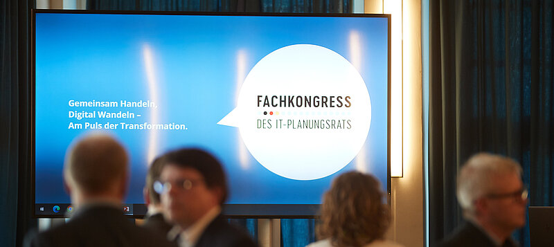 Bildschirm mit dem Fachkongress-Logo, davor Menschen