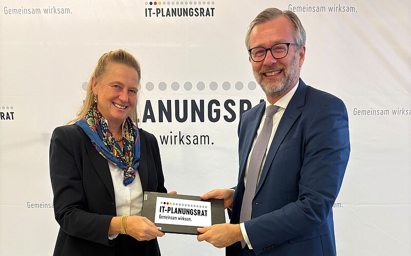 Foto von Dr. Geue und Prof. Dr. Hölscher, die beide ein iPad mit dem eingeblendeten Logo des IT-Planugnsrats in den Händen halten