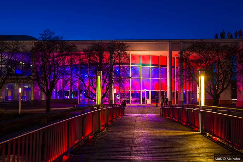 Die Rotunde der Musik- und Kongresshalle Lübeck (MUK) erstrahlt bei Nacht in bunten Farben. 